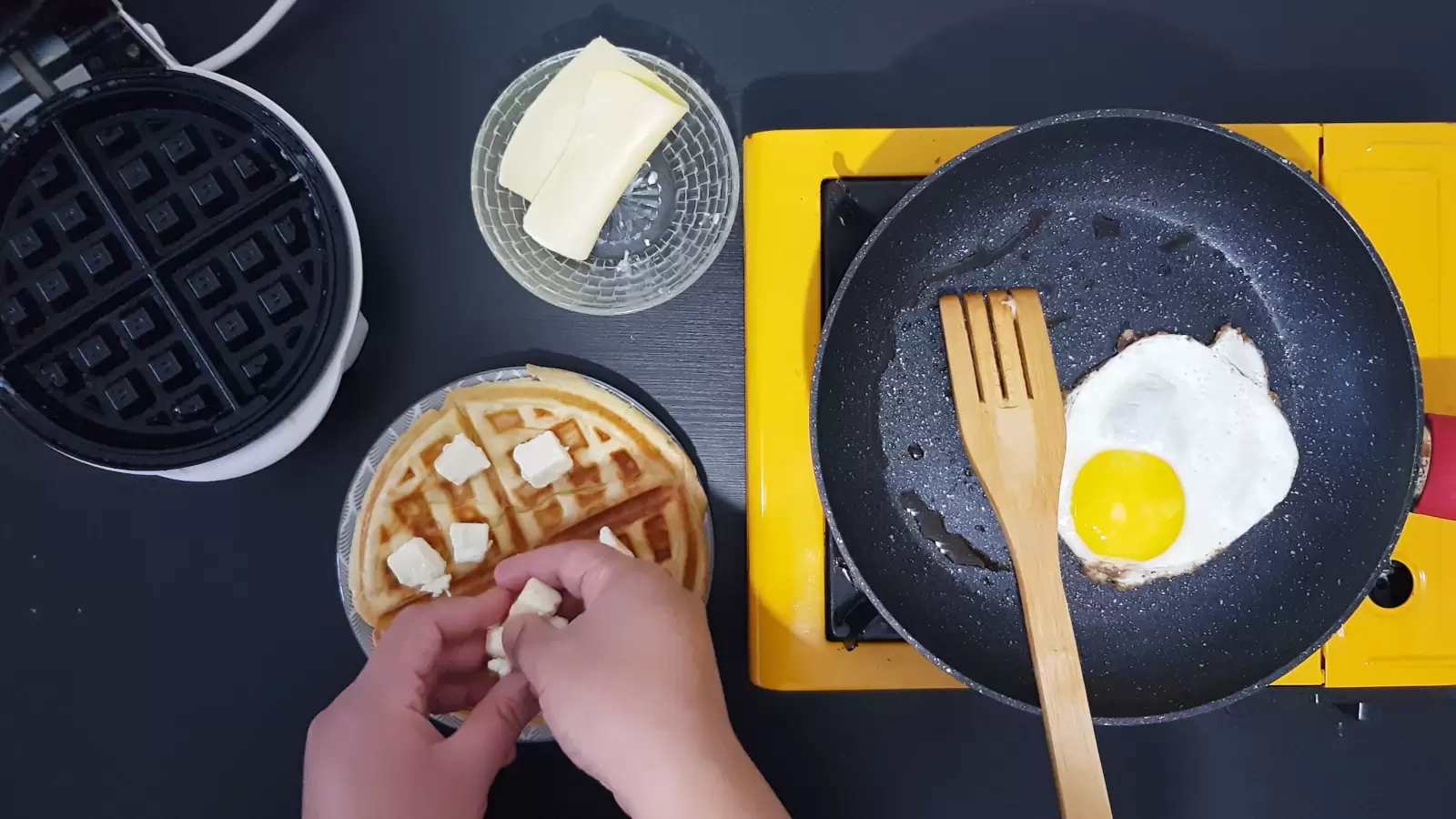 Egg in a pan. Cheese in a bowl. Belgian waffle with cubes of butter.