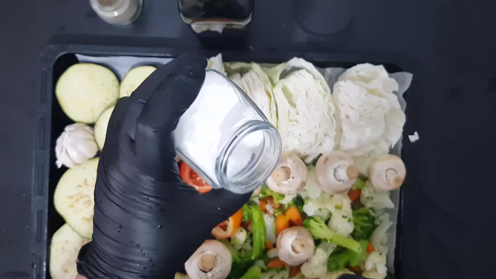 A tray for the oven with vegetables, a jar of salt