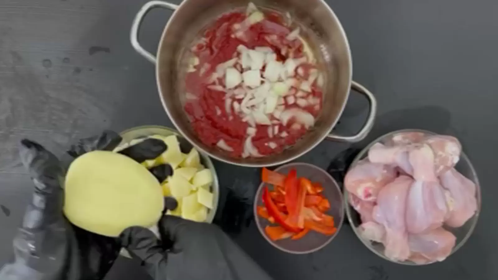 A bowl with chicken thighs, a bowl with 4 potatoes, a pot with tomato and onion sauce, a bowl with red pepper