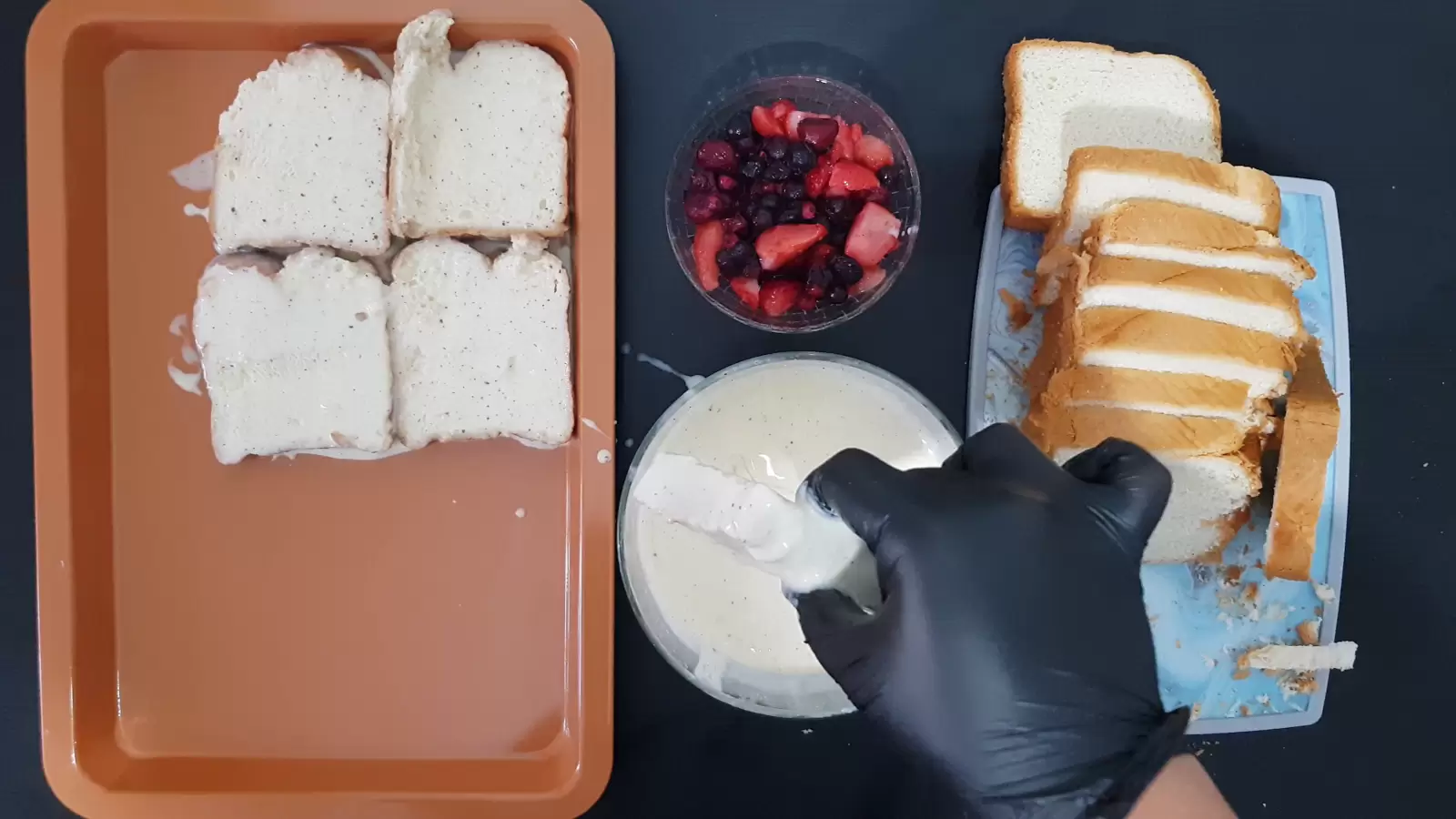 Sliced ​​bread on cutting board, bowl with berries, bowl with batter and bread dipped in it, baking pan with bread dipped in batter