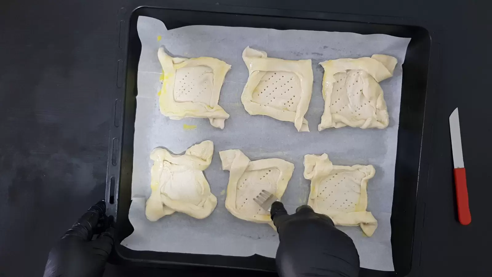 Puff pastry ready on a baking sheet, fork making holes in the center of the pastry.