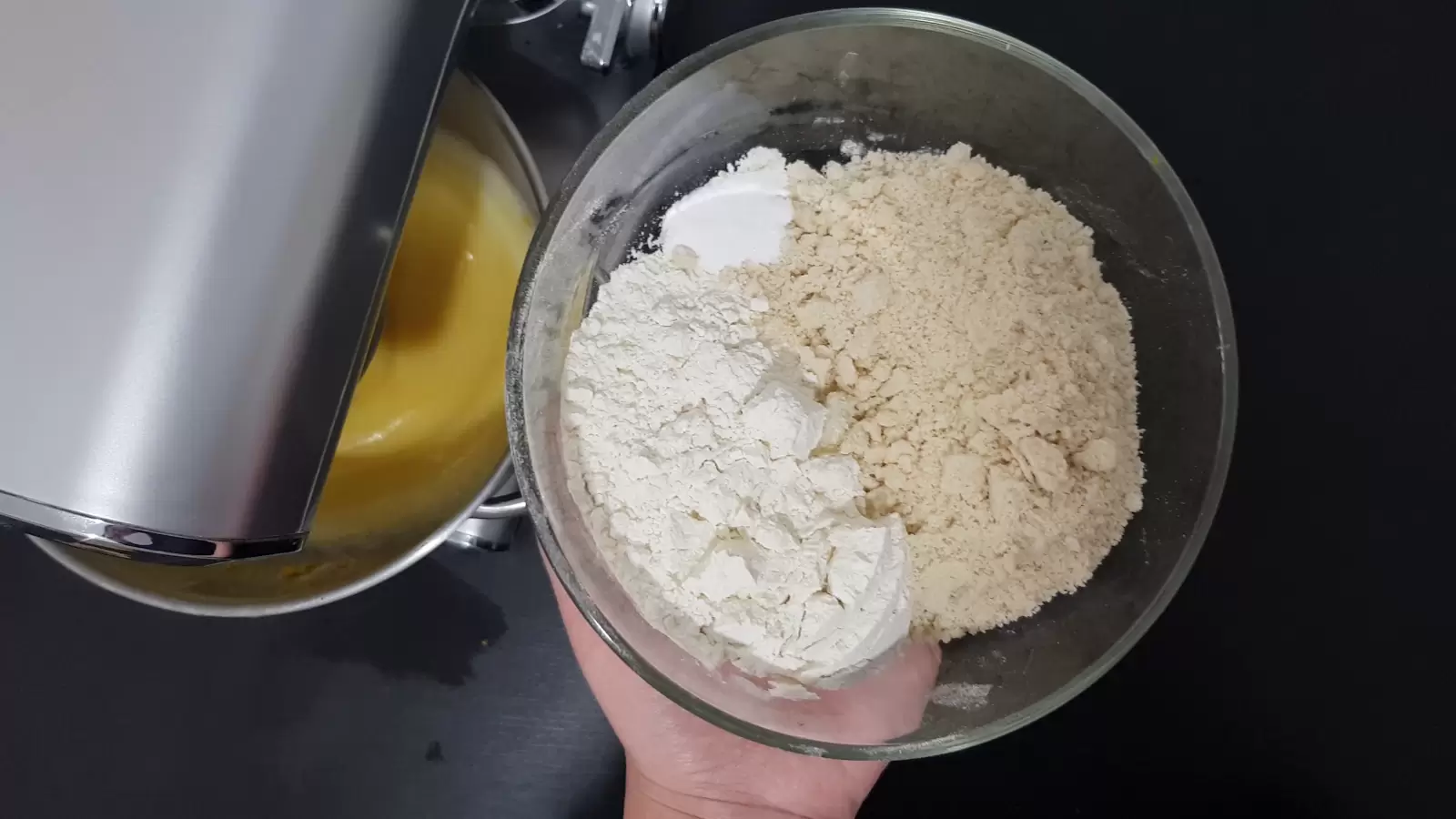 A mixer with a batter, a bowl with flour, baking soda and almonds