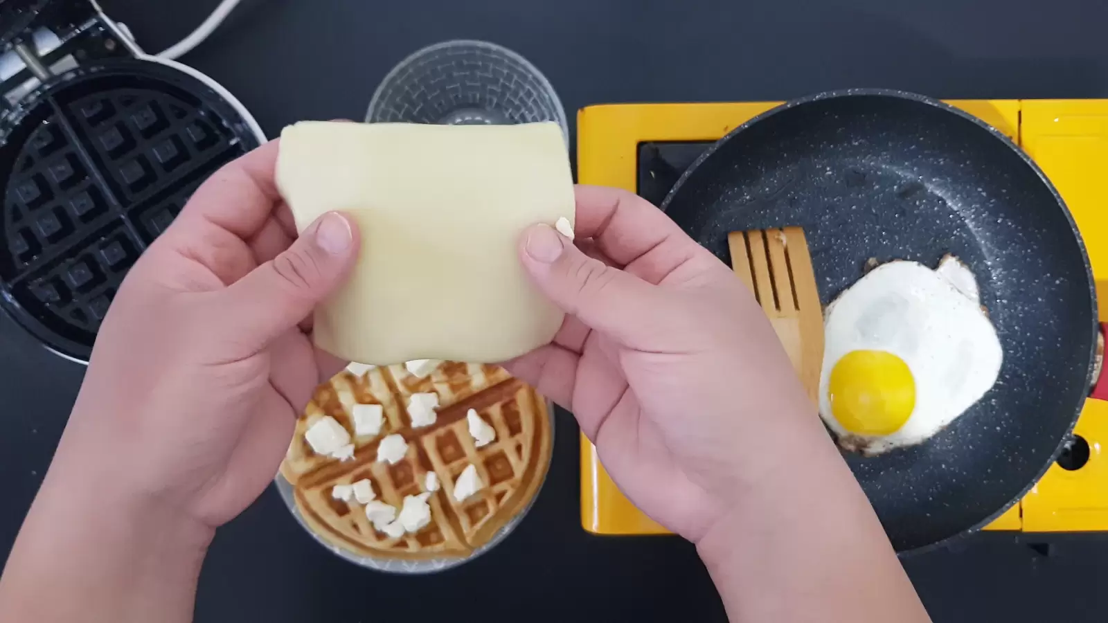 Egg in a pan. A slice of cheese. Belgian waffle with cubes of butter.