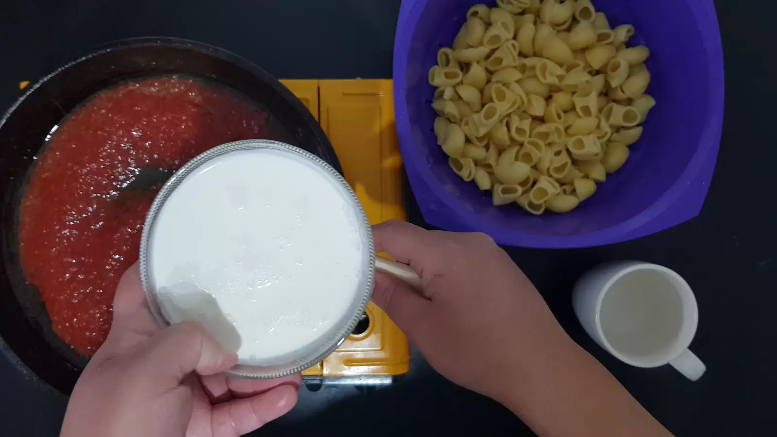 A glass, a bowl with pasta, a bowl with whipped cream, a pan with tomato sauce