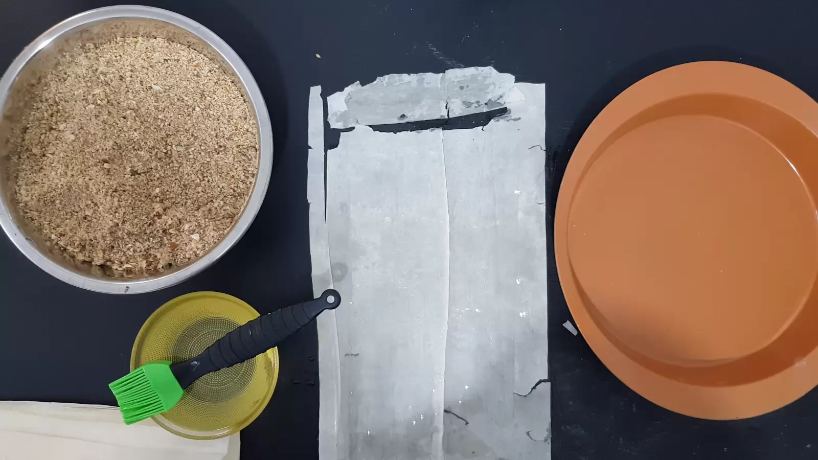 An oven tray, phyllo sheets, a bowl with oil and a brush for spreading, a bowl with a mixture of chopped nuts