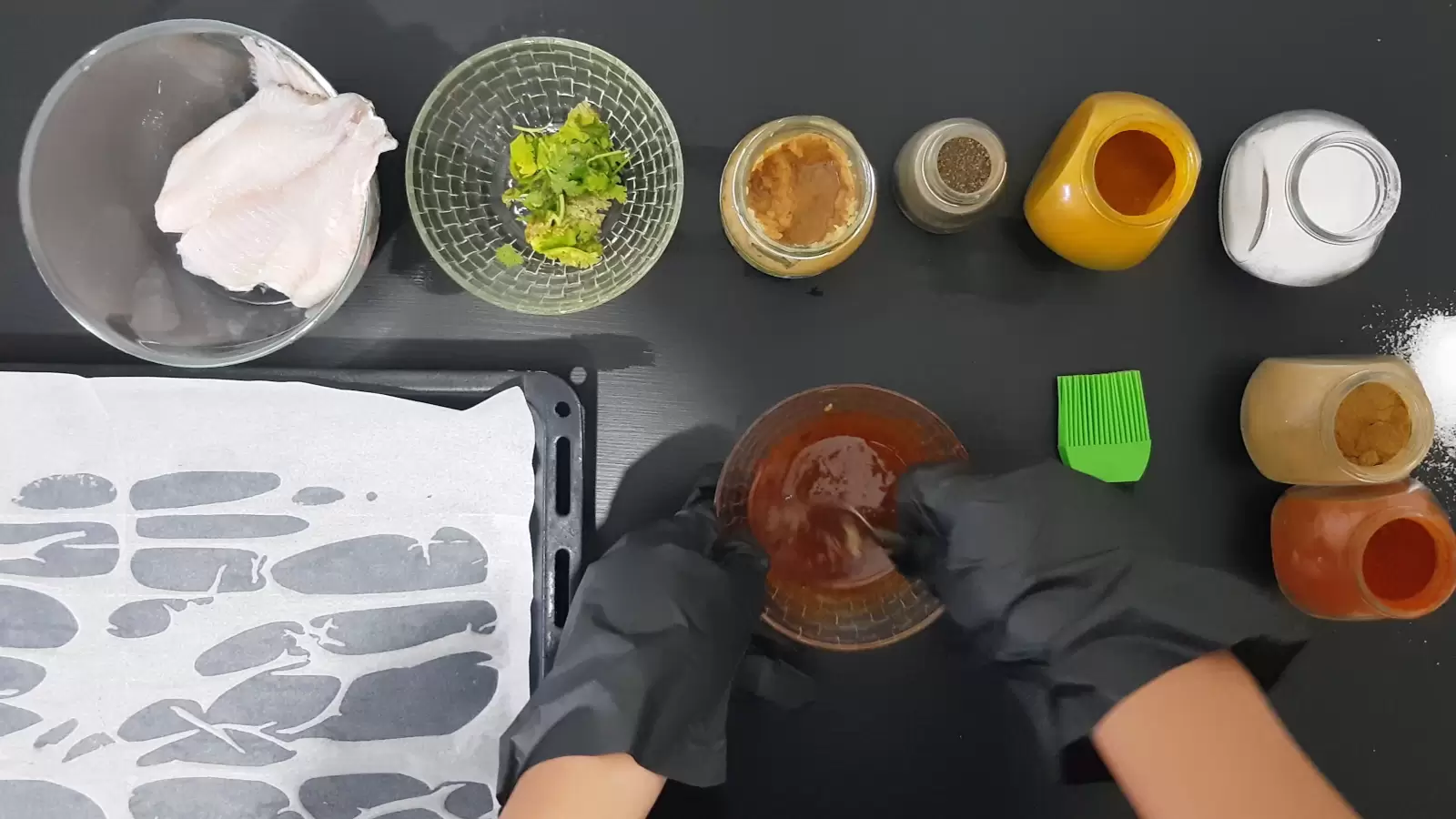 Turmeric, paprika, cumin, pepper, salt, coriander, oven tray, tilapia fish, brush, spoon mixing in a bowl