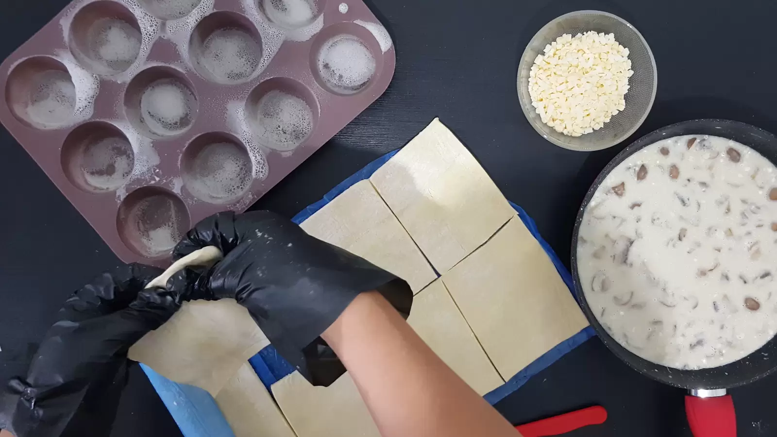 Pan with mushroom and cream filling, bowl with grated cheese, filo dough divided into squares, muffin tin greased with spray