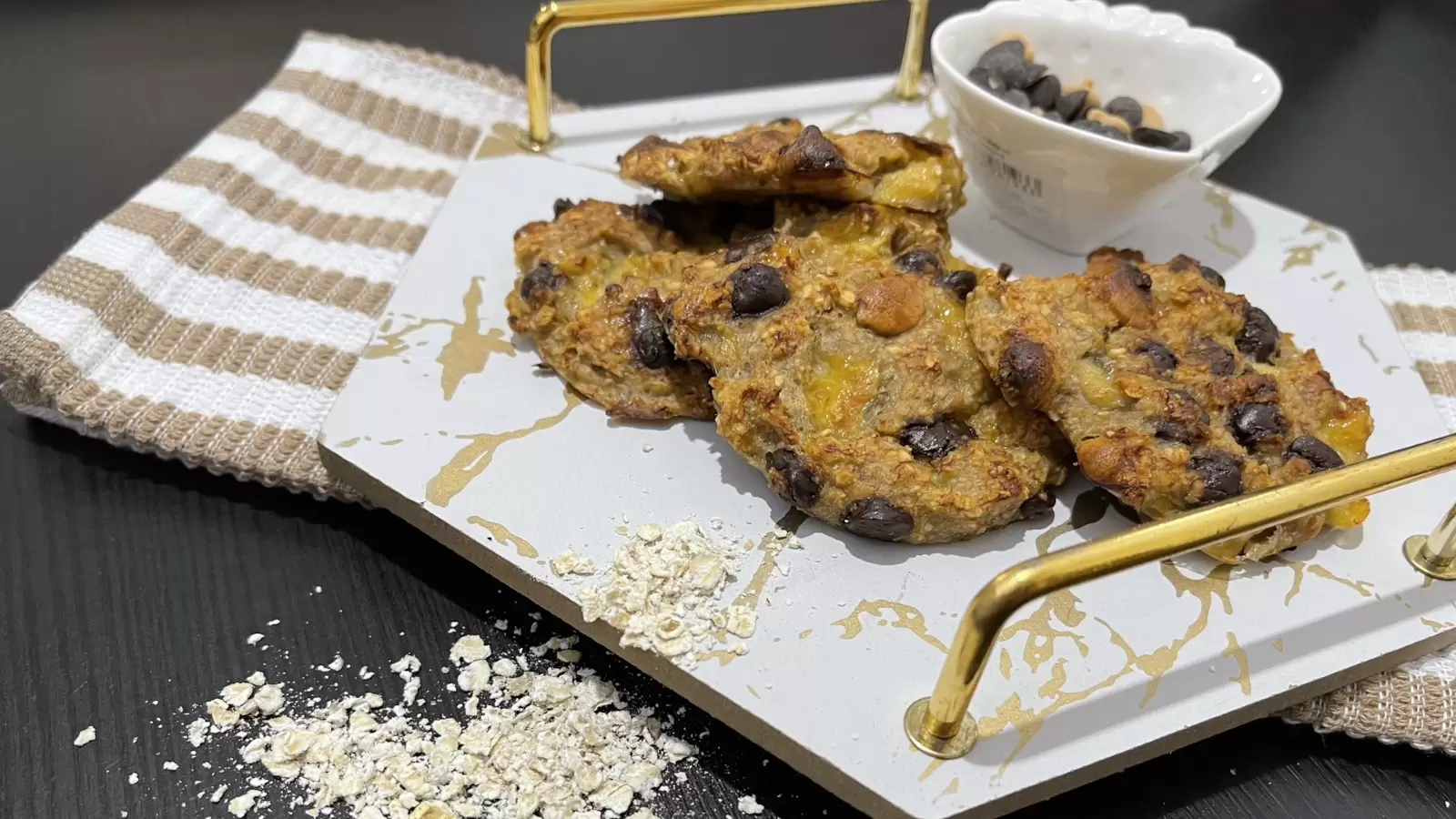 Tasty Banana and oatmeal cookies on a tray a bowl of chocolate chips oatmeal scattered on the table