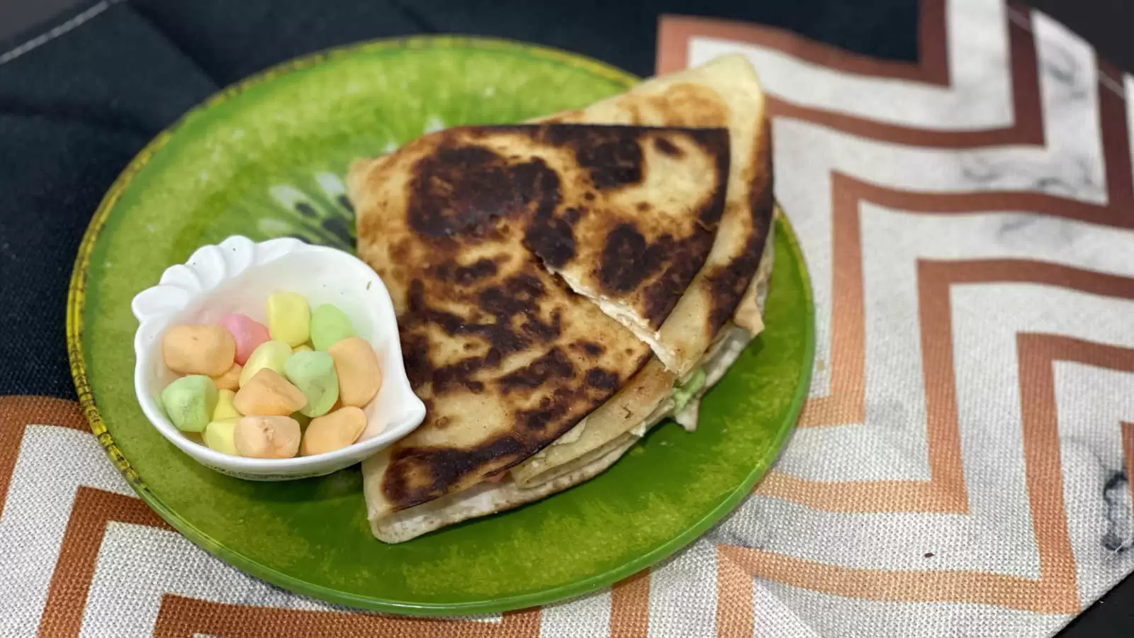 Tortilla Smores dessert on a plate a bowl with marshmallows on a green plate on a striped napkin