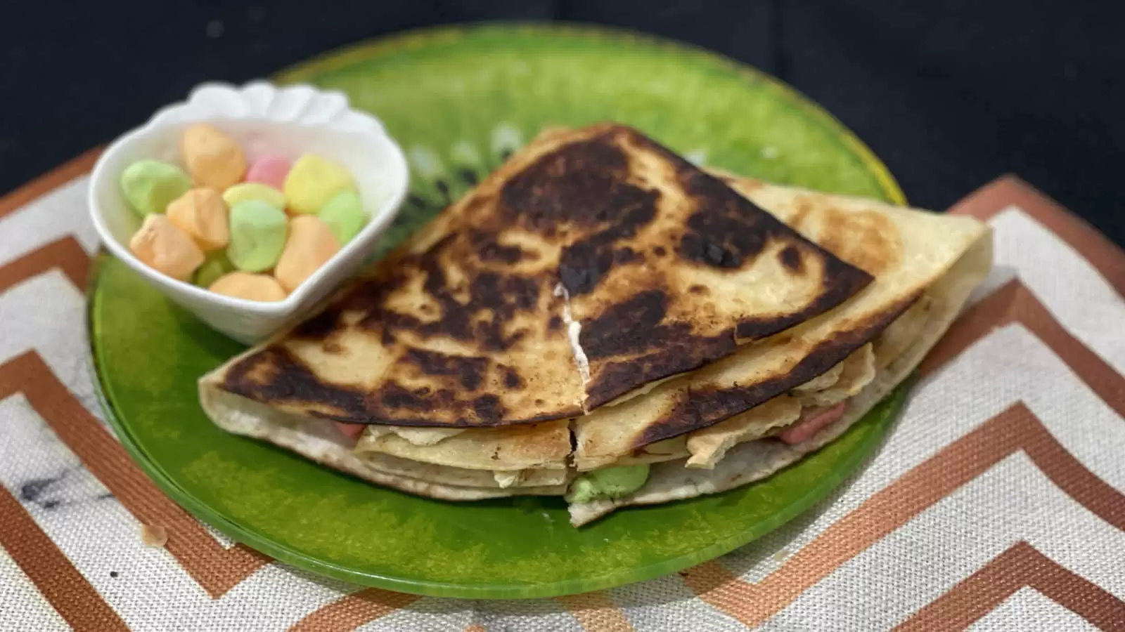 Tortilla Smores dish on a plate a bowl with marshmallows on a green plate on a striped napkin