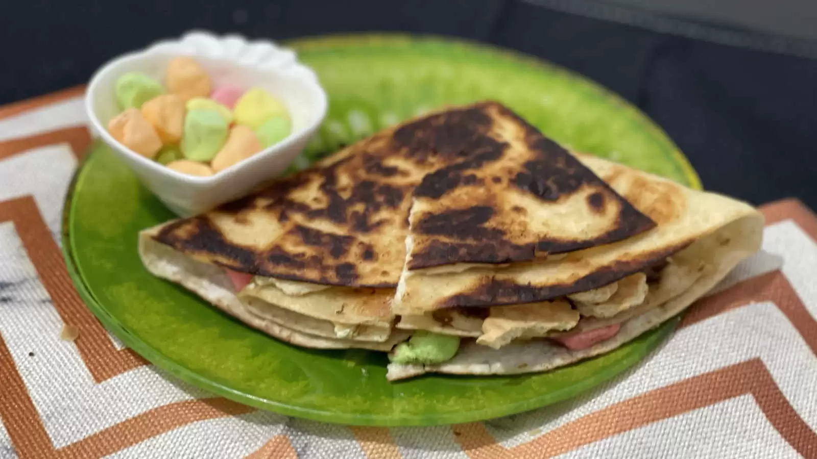 Tortilla Smores recipe on a plate a bowl with marshmallows on a green plate on a striped napkin